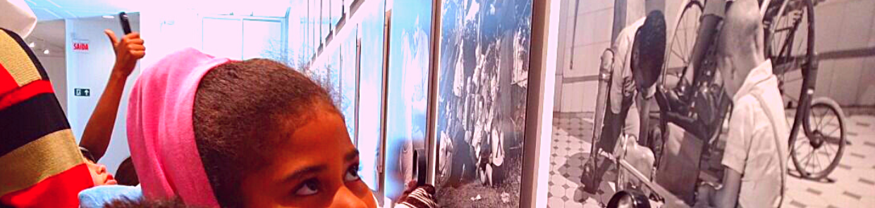 olhar de uma criança negra observando o quadro de uma fotografia com crianças, preso na parede